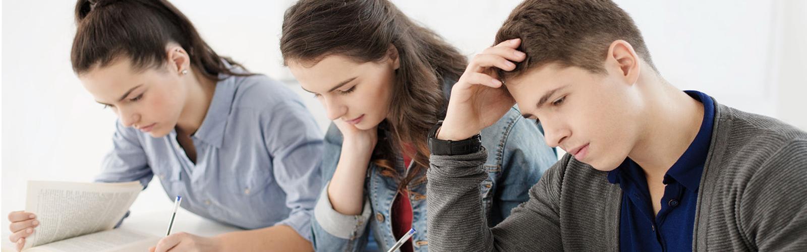 Three students sitting next to each other at a table each looking at a textbook